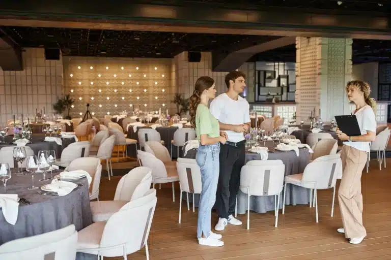 Coppia visita una location per eventi con una consulente in una sala elegante allestita per un ricevimento