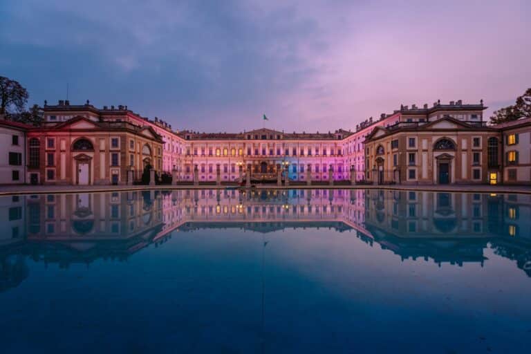 Villa storica neoclassica illuminata di sera con grande corte riflessa sull’acqua