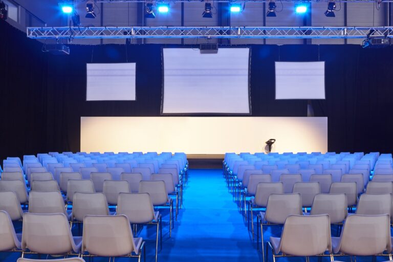 Sala conferenze allestita con sedute, palco e schermi per una convention aziendale